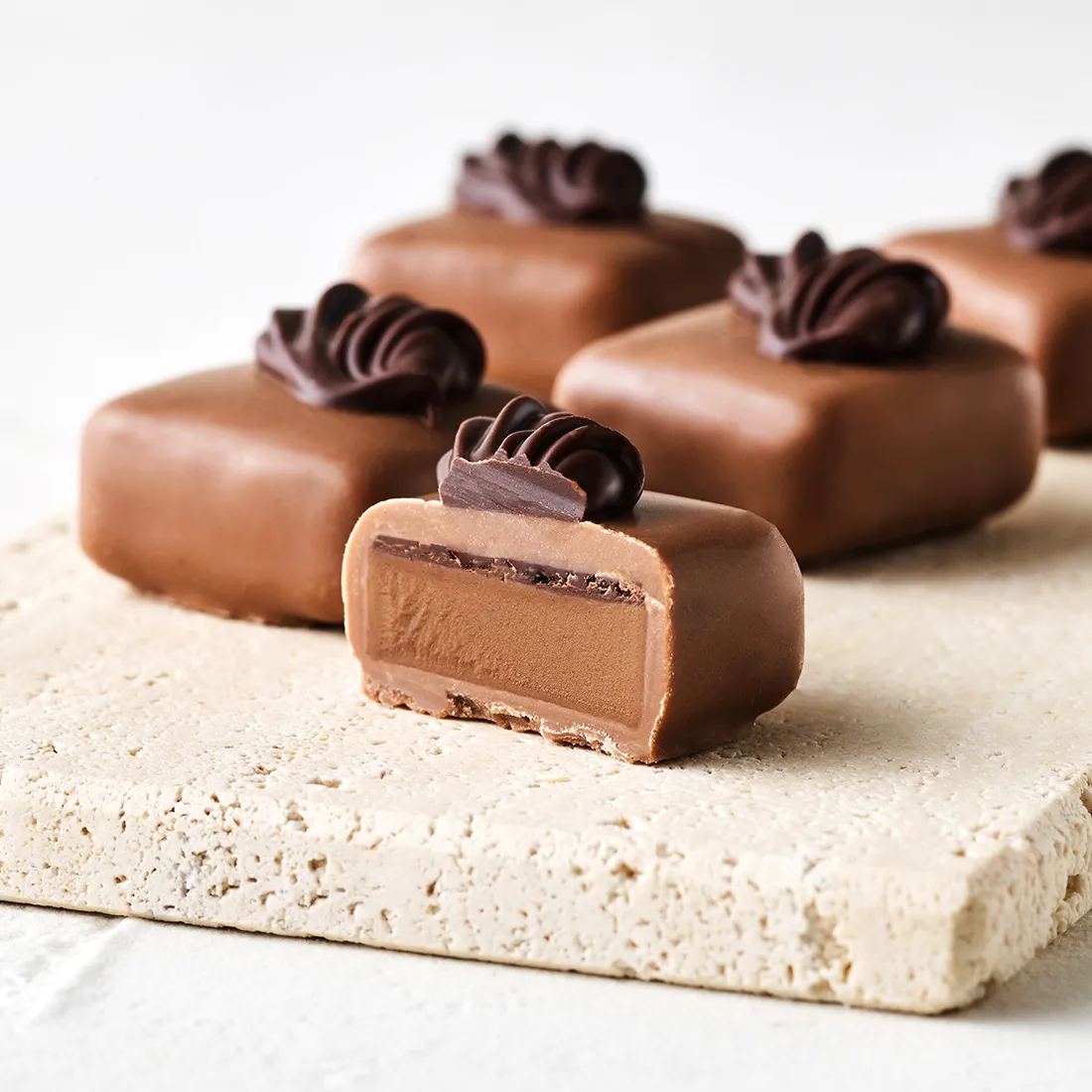 Nussbitter-Nougat Vollmilch, 6 St. Stimmungsbild: Nussbitter-Nougat Trüffel in Vollmilchschokolade mit Zarbitterschokoladen-Dekor appetitlich angeschnitten