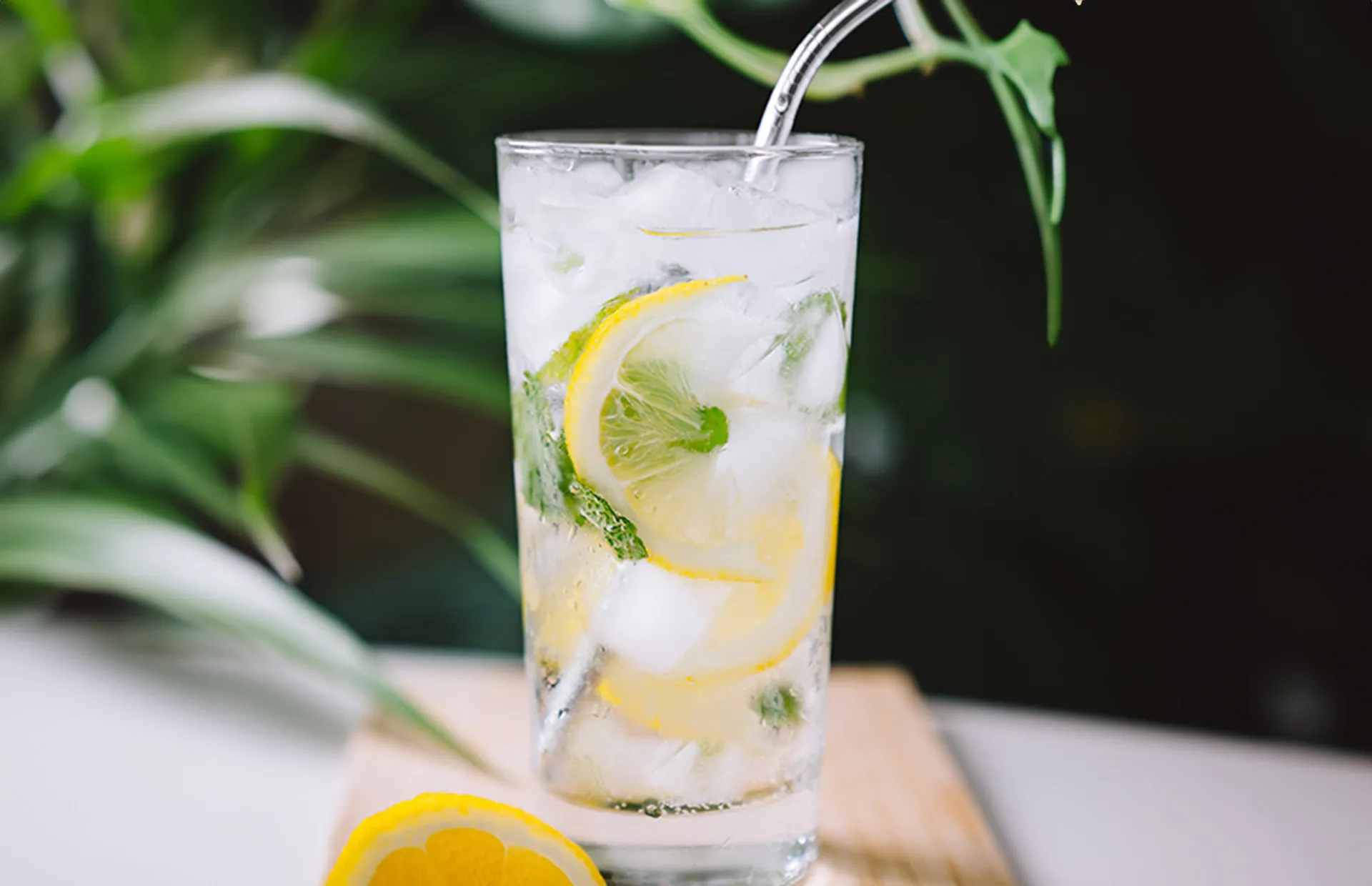 Stimmungsbild: Glas mit Ingwersirup Zitronenschalen und Strohhalm auf Eis