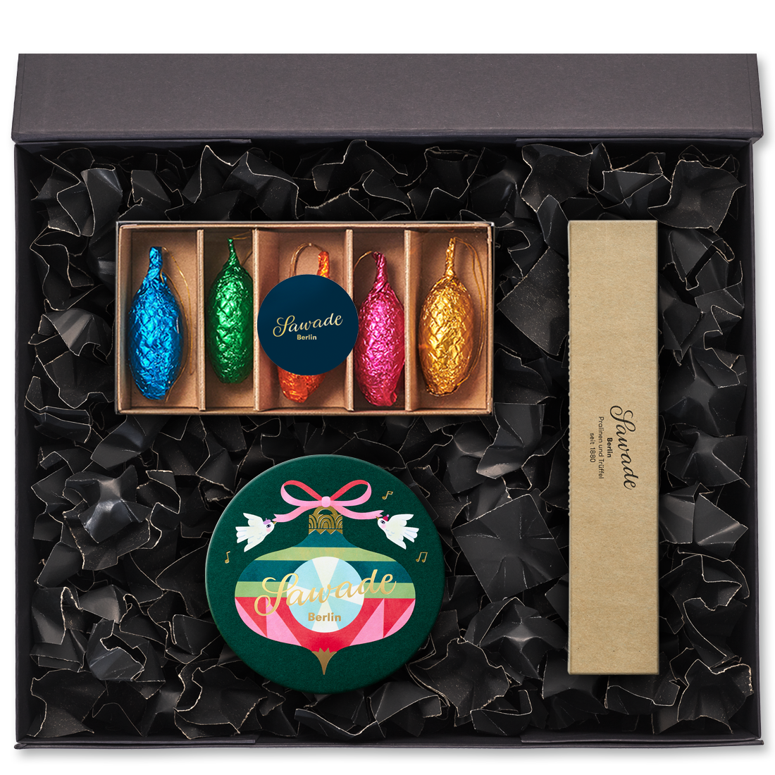 Geschenkbox offen mit einer kleinen Schachtel Baumschmuck, einer Runddose Schmuckstück und einer Pralinenstange Blätterkrokant